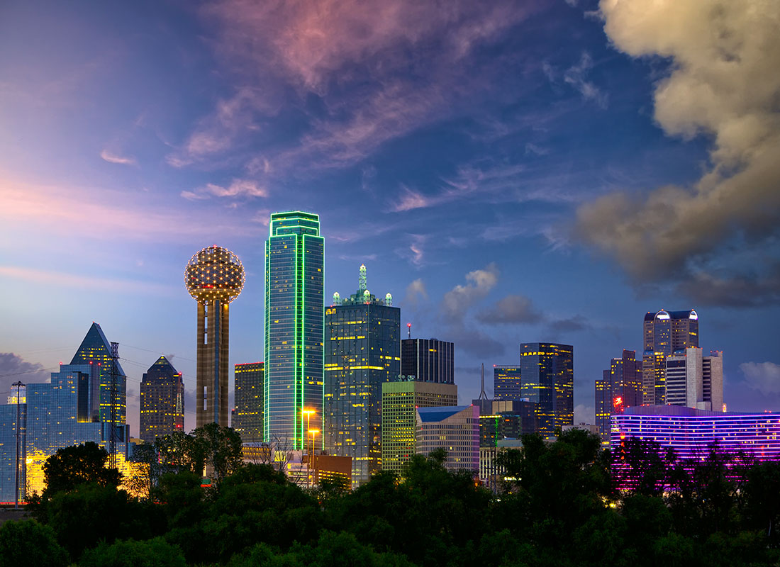 About Our Agency - Buildings in Downtown Dallas Texas in the Early Evening with the Lights On Against a Colorful Sky